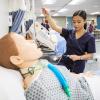 A student holds up an IV line that’s attached to a training dummy.