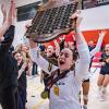 A volleyball player holds a trophy above their head while their teammates cheer.