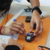 A student uses a tool on a mechanical device while another student looks at schematics.