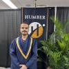 A person wearing convocation robes stands in front of a Humber Polytechnic banner.