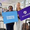 Two people stand beside suitcases holding signs that read Humber Global Summer School and Humber.