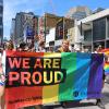 People march in a parade while holding a rainbow-coloured banner reading We Are Proud and Humber.