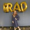 Emma Kilgannon wears a convocation gown and stands beneath balloons that spell out the word grad.