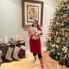 Jessica Rotolo holds socks bearing her winning design while wearing a pair of the socks and standing next to a Christmas tree.