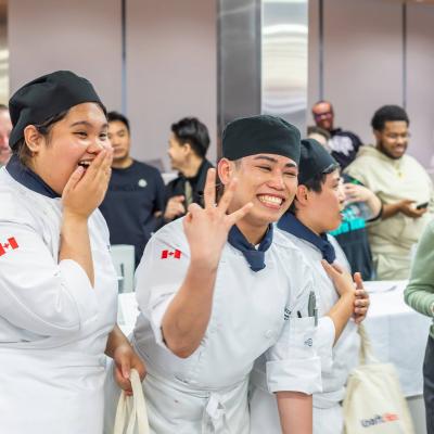 Three people wearing chef outfits celebrate after being named the winners of the Kraft Heinz Iron Chef competition.