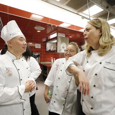 Several instructors wearing chef's uniforms speak to each other in a kitchen.
