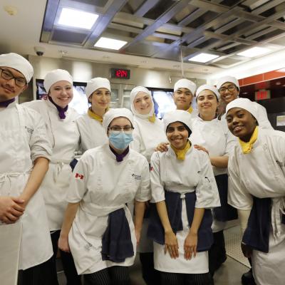 A group of 10 students wearing chef's uniforms pose for a photo.