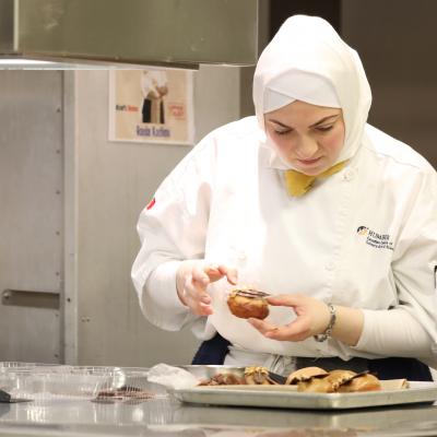 A person wearing a chef's uniform works on a dessert.