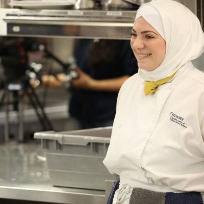 Roula Kadimi smiles and is wearing a chef's uniform.