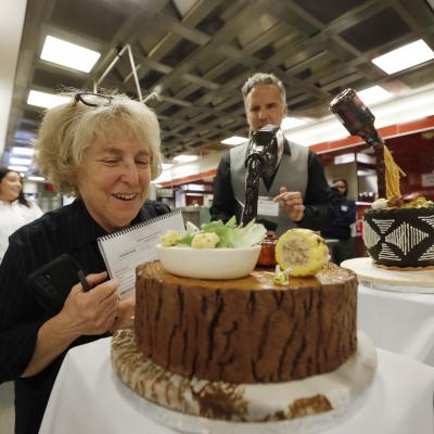 A judge looks at a gravity cake made to resemble a barbecued steak with Caesar salad and corn on the cob.