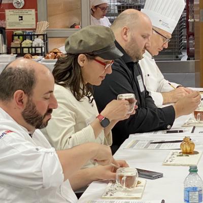Four judges sitting in a row sample a dessert.