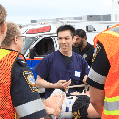 A person speaks to students while standing over a mock patient.