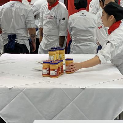 Students wearing chef's outfits pick up jars of Cheez Whiz.