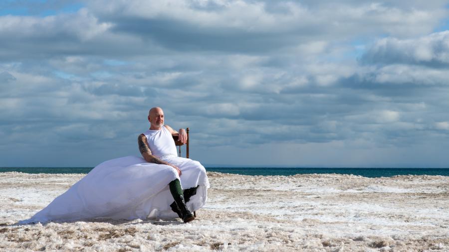 'Raise Hell' by Madeline Wallace is a photo of a person with a beard and a long white dress on a windy day at the beach