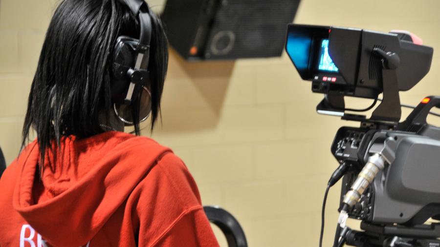 A Humber student operates a video camera with headphones on