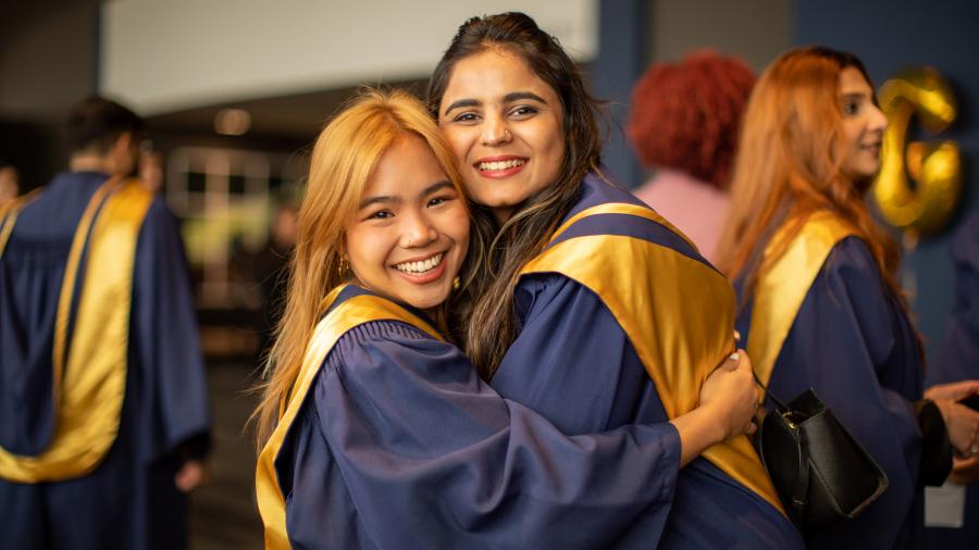 Two people wearing graduation gowns embrace at Humber College’s Fall Convocation.
