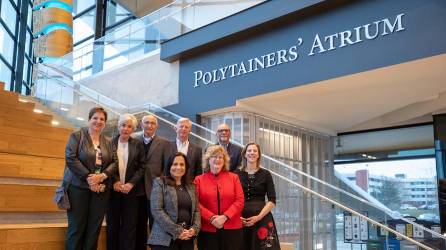 Eight people stand on steps beneath a sign that reads Polytainers’ Atrium.