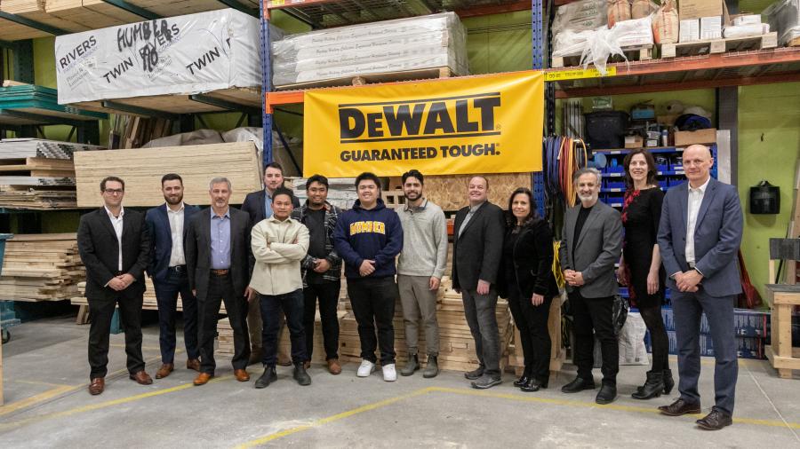 A group of people stand underneath a sign that reads DEWALT Guaranteed Tough.
