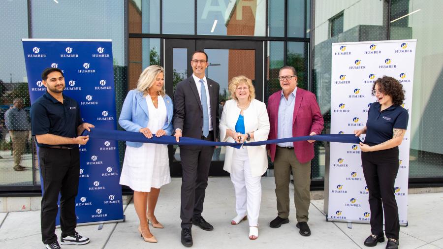 Four smiling people prepare to cut a ribbon being held by two people wearing Humber shirts.