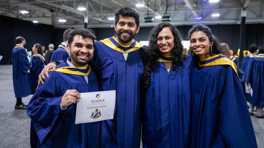 Four smiling people wearing graduation robes.