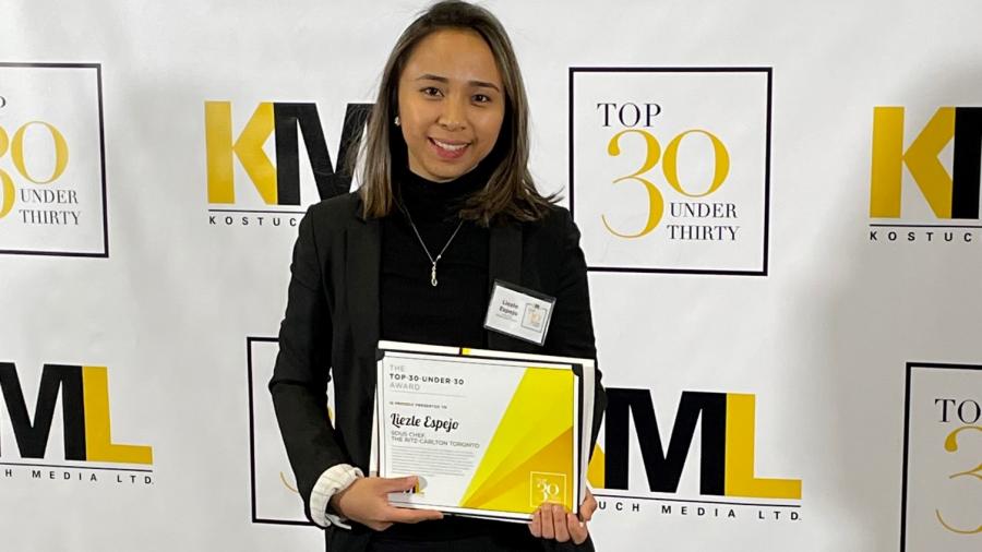 Liezle Espejo holds a certificate while standing in front of a sign that reads Top 30 Under Thirty.