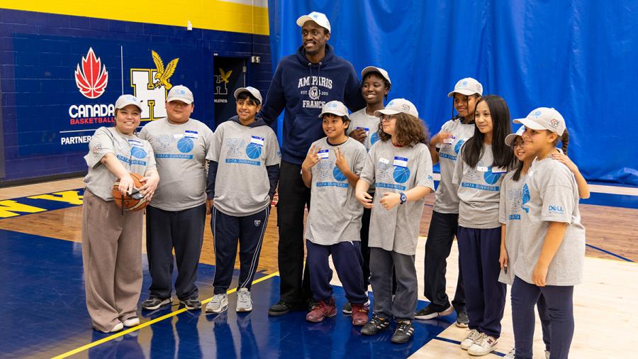 A person stands with a group of youth who are wearing the same grey t-shirts in a gym.