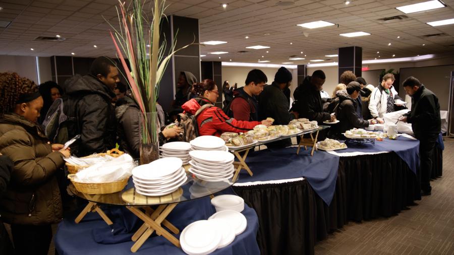 People line up to serve themselves food from a table while holding plates and cutlery.