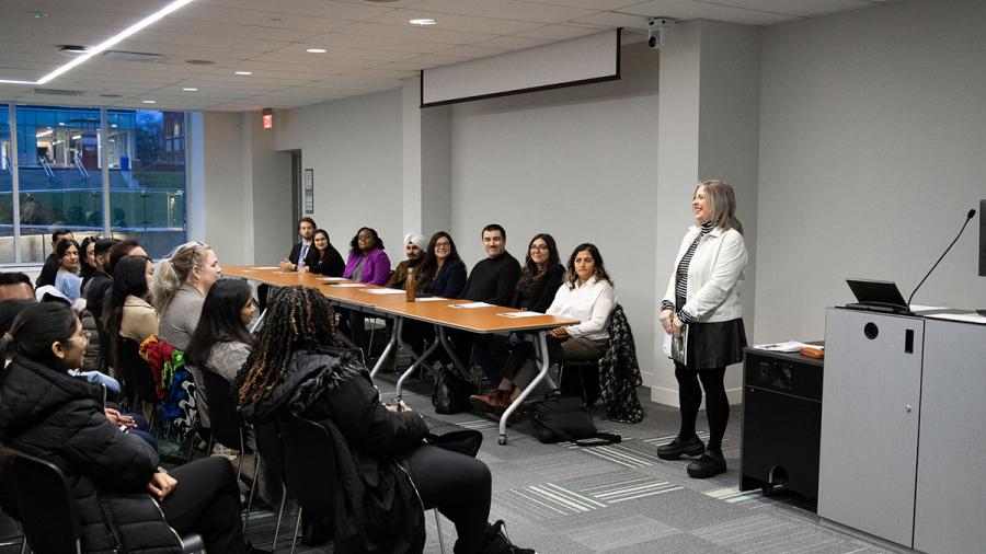 A person standing at the front of a room is speaking to an audience that is watching and listening.