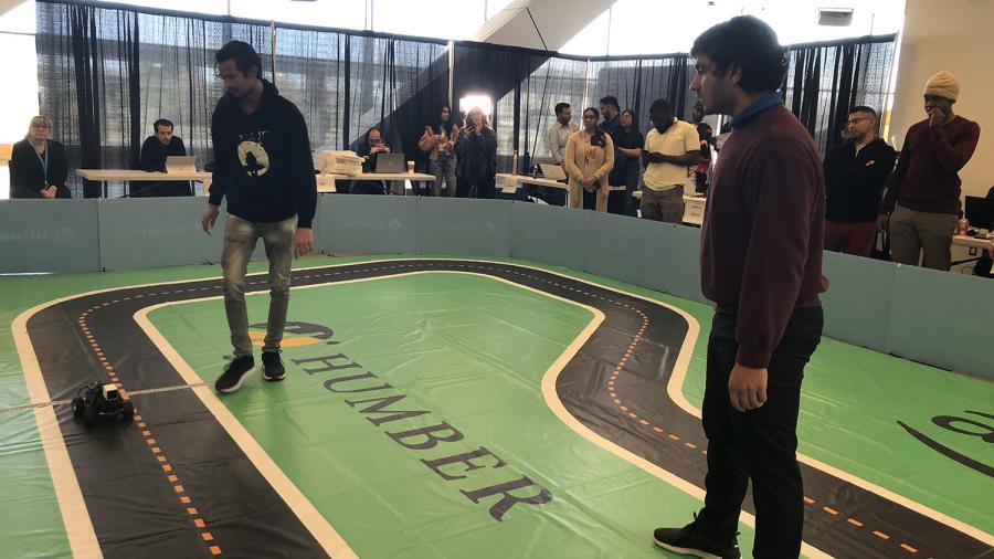 Two people stand on a miniature track while a car navigates the course.