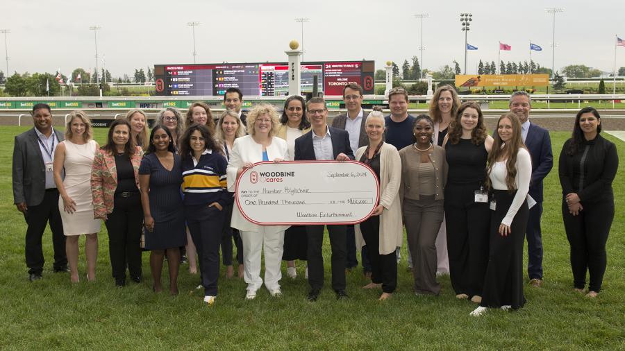 A group of people stand on a racetrack while three people holding a large cheque made out to Humber Polytechnic.