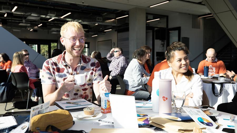 Smiling people sit at a table that’s covered in paper and other items.