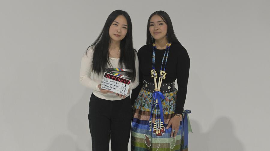 Two people stand together against a grey backdrop.