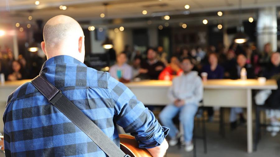 A person plays a guitar on a stage while the audience watches.