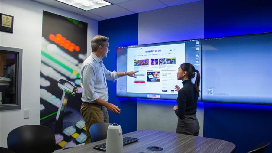 Two people stand in front of a screen while having a discussion.