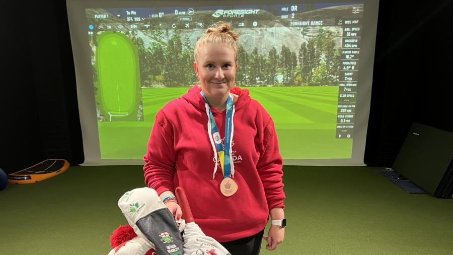 A golfer wears a bronze medal around their neck while standing in front of a golf bag filled with clubs. 