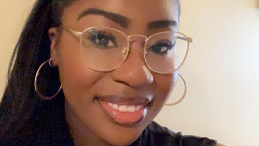 Michelle Ntiamoa smiles in a selfie. She is wearing nude lipgloss and large wire-framed glasses