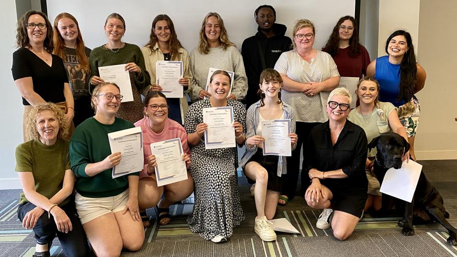 A large group of smiling people pose for a photo while holding certificates.