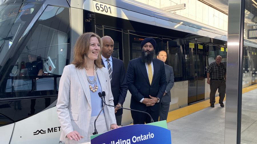 Several people stand in front of an LRT train and behind a podium that reads Building Ontario.