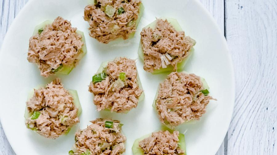 Several tuna sliders arranged on a white plate on a white table. The sliders are pink with tuna mixed with green onions