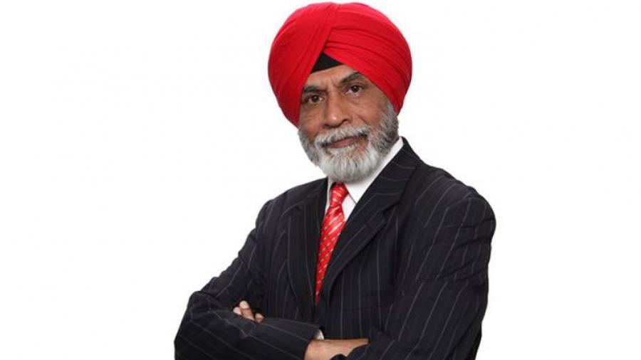 Baldev Mutta stands with arms crossed, wearing a black suit and red turban
