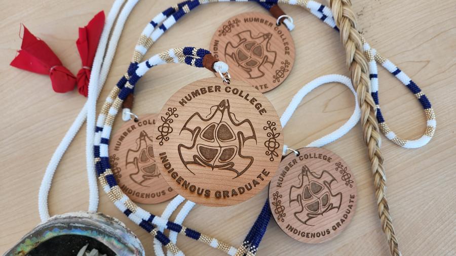A collection of medallions that read Humber College Indigenous Graduate sitting on a table.