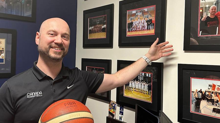A person holding a basketball points towards framed photos on a wall.