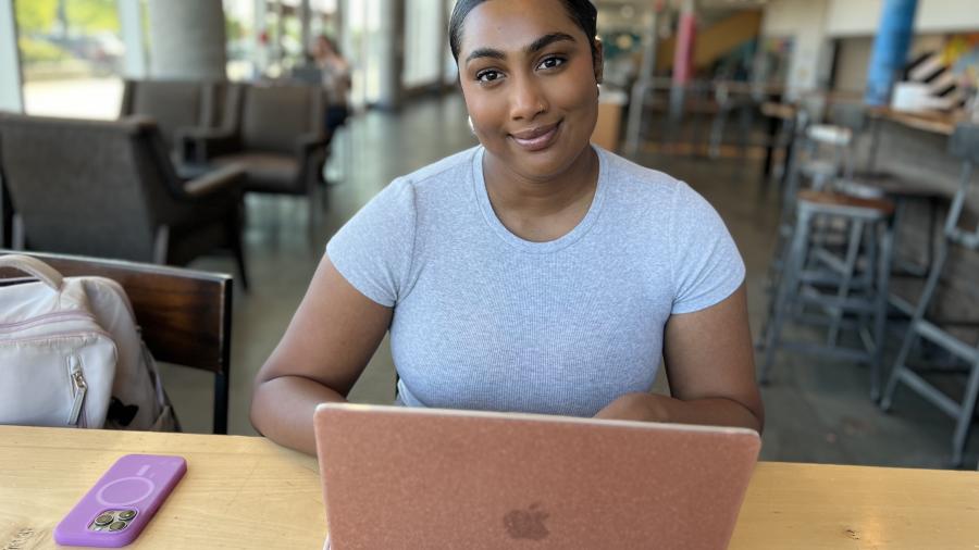 A smiling person sits in front of a laptop computer.