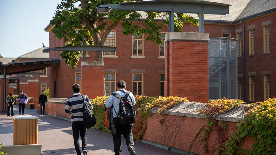 Two students walk together past a building.