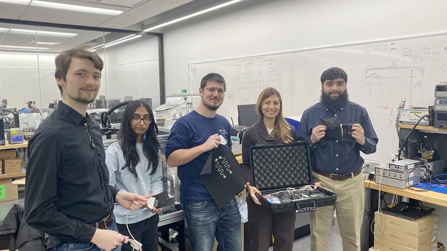 Several people stand together in a lab holding up pieces of technology.