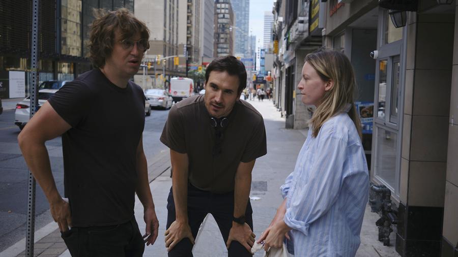 A person stands between two people while resting his hands on his knees.