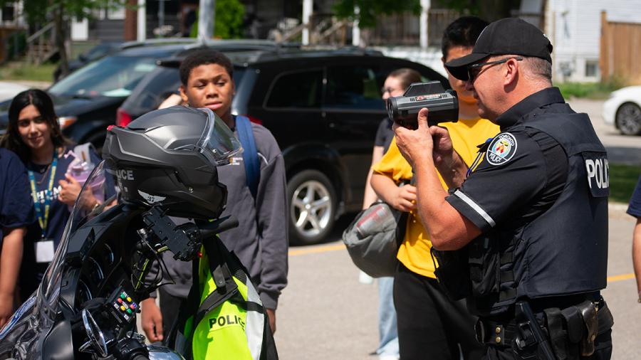 A police officer holds up a speed camera as youth look on.