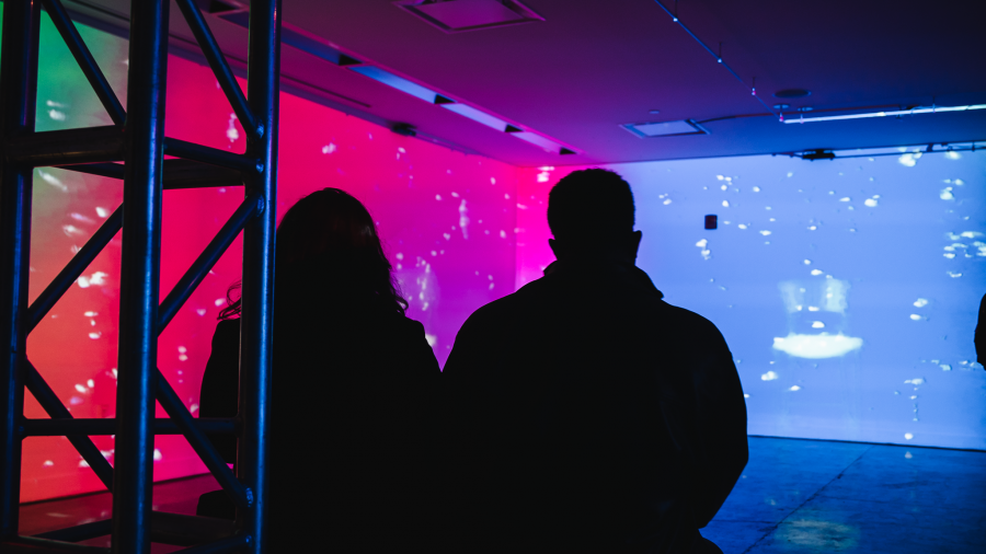 Two people look at varying colours and shapes being projected on walls.
