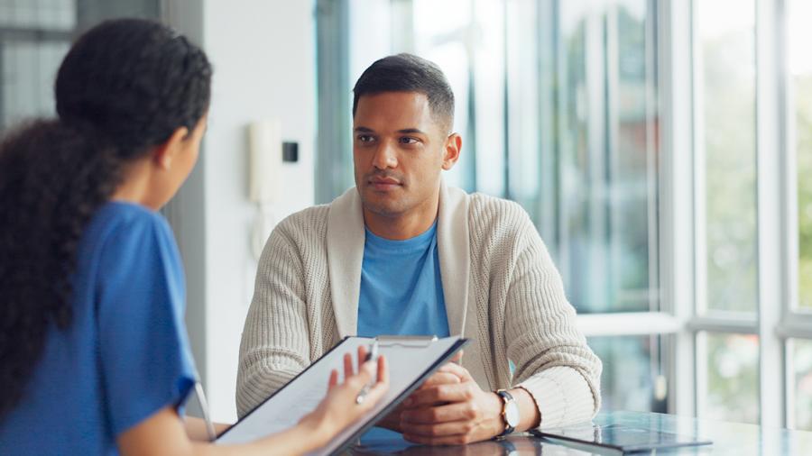 A person wearing nurse’s scrubs speaks with another person sitting with them at a table.