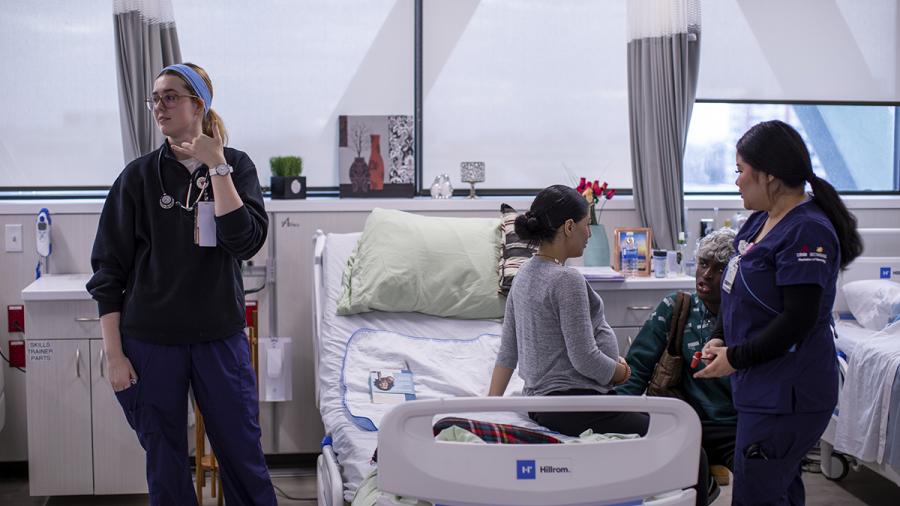 Nurses stand next to a hospital bed that a patient is sitting on.